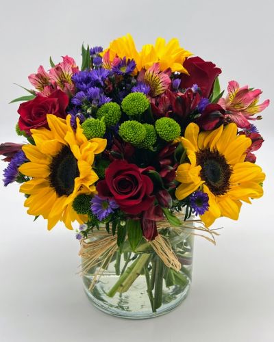 Reminiscent of strolling through a field of flowers, this colorful arrangement captures features magnificent sunflowers, alstroemeria and poms set in a trendy mason jar with a natural raffia bow.
<ul>
<li>Our florists hand-design each arrangement, so colors, varieties and containers may vary due to local availability</li>
</ul>